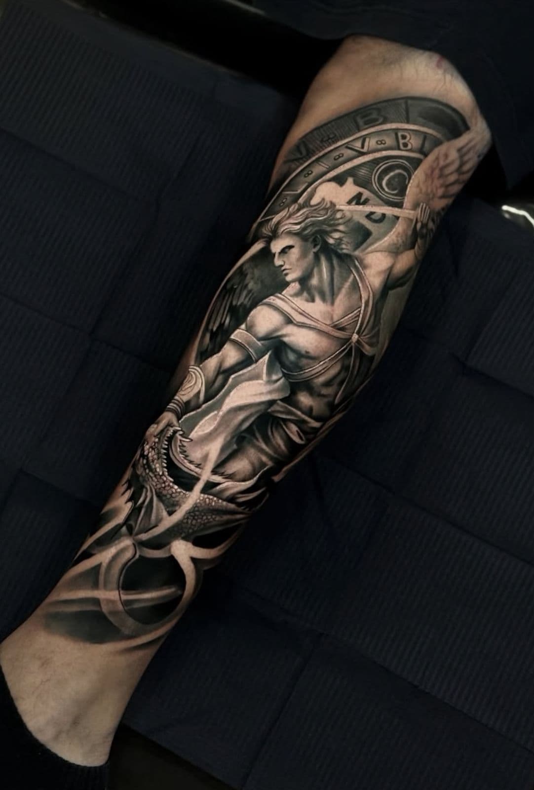 Tatuagem realista de anjo guerreiro com dragao e relogio na perna